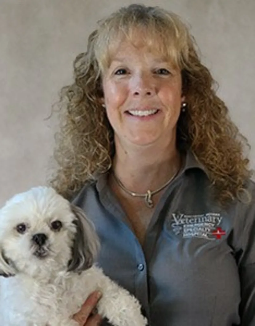 Dawn Slessman smiling in front of a grey backdrop holding a small white dog